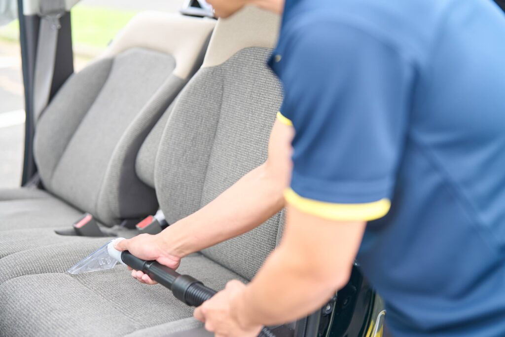 店長が車のシートをリンサークリーニングしている画像。アルカリ電解水とスチームなどを使い、シートに染み込んだ汚れを浮かし、リンサー洗浄（水洗いして吸い取り）します。